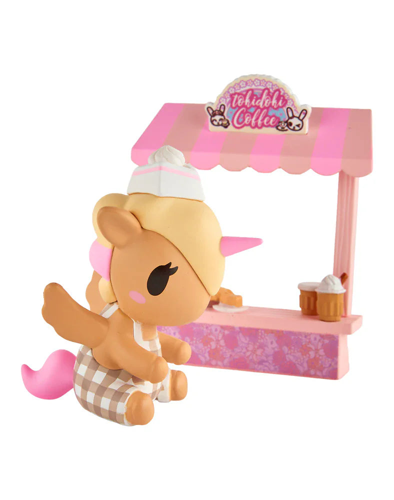 The tokidoki Farmers Market Unicorno - Cafe Cuties Coffee Bar (Special Edition) figurine features a Unicorno with a hat and apron in front of a pink-striped coffee stand with cupcakes and a