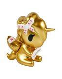 A charming Fortune Cookie Unicorno from Tokidoki sits with closed eyes, wearing a white bow with red symbols and holding a fortune slip—get this surprise figure in the Fortune Cookie Unicorno Blind Box!.