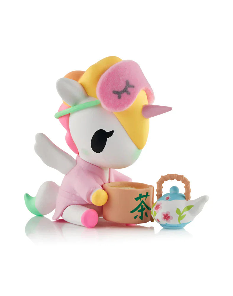 Add kawaii wellness to your space with Tokidoki's Spa Day Unicorno Blind Box, featuring a pastel-colored Unicorno in a pink robe and sleep mask, sitting with a teacup and floral teapot on a crisp white background.