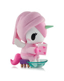 A Tokidoki Spa Day Unicorno Blind Box figurine with pink hair and a towel relaxes on a bench, holding a heart book and dipping its feet in a glass bowl for the ultimate kawaii wellness vibe.