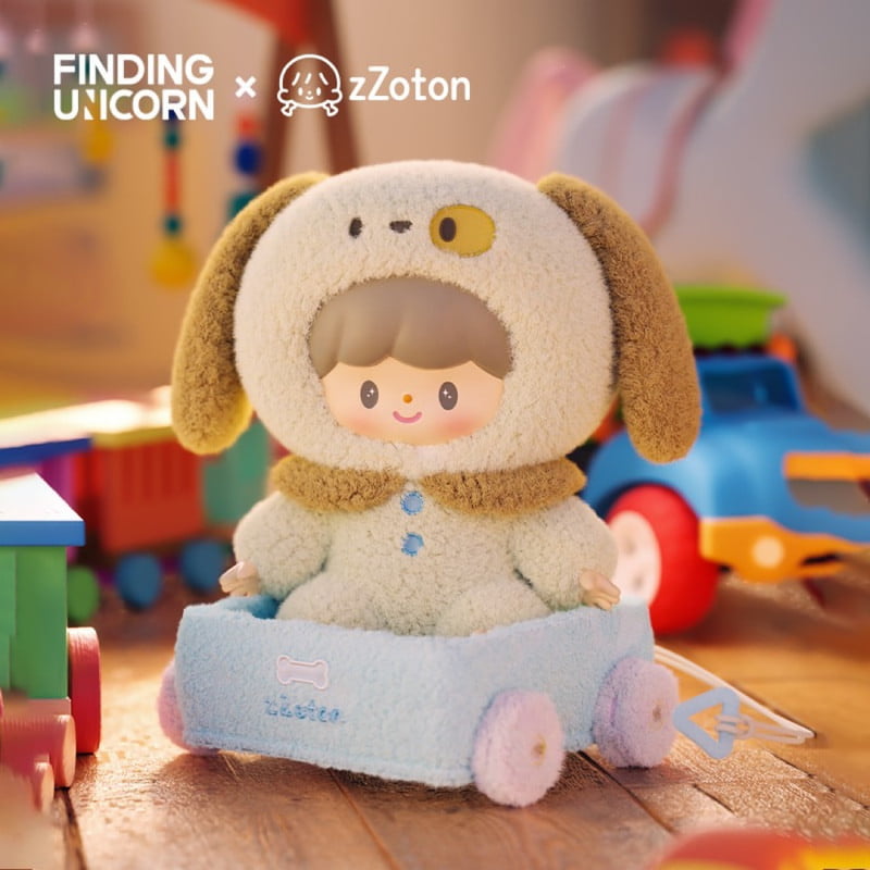 A zZoton doll from Finding Unicorn's Happy Childhood Blind Box, dressed in a fluffy dog costume, sits in a blue toy cart surrounded by colorful collectible figures, trains, and cars in a playful room. Branding appears at the top left.