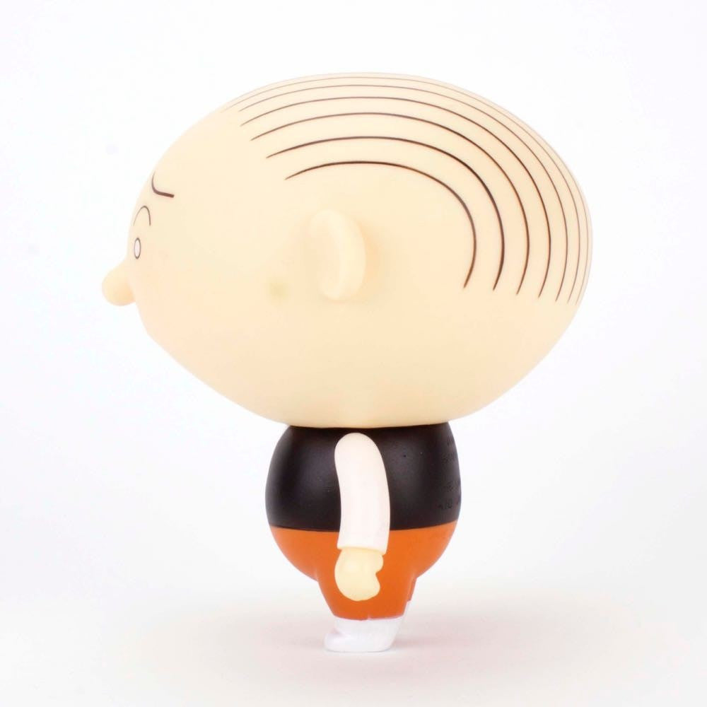 A side view of the Jimmy Corrigan Vital Animus Vinyl Doll by Presspop (JP)—a cartoonish figure with a large bald head, black lines for hair, black vest, white shirt, orange pants, and white shoes inspired by Chris Ware’s acclaimed comics.