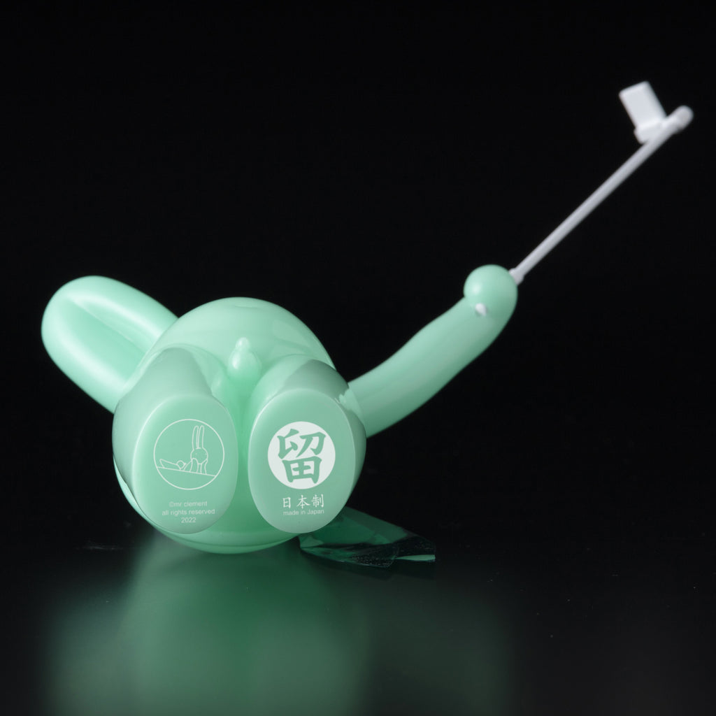 A green toy elephant adorned with The Daily Flasher by mr. clement is holding a toothbrush.