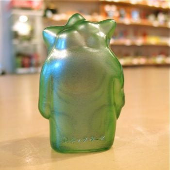 A Popsoda Finger Puppet - Clear Green, reminiscent of a kaiju, sits on the table.