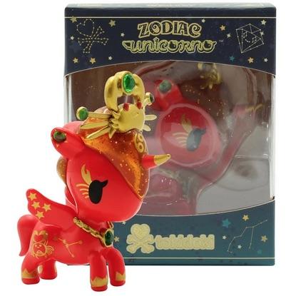 In front of a box sits a red Zodiac Unicorno — Cancer toy, adorned with a golden hat by tokidoki.