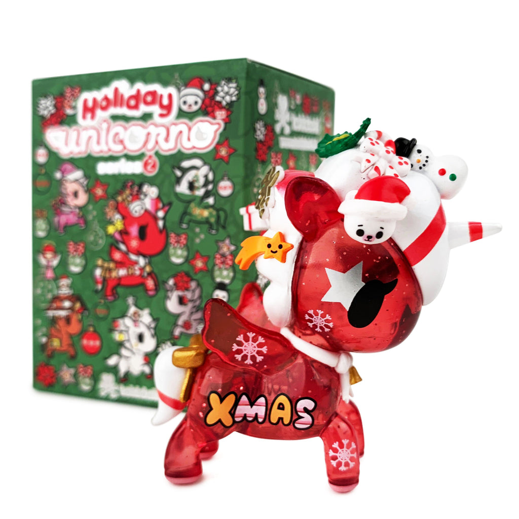 A transparent red unicorn figurine with festive décor stands before a green tokidoki Holiday Unicorno Series 2 Blind Box, resembling one of the charming ornament-style chase figures from this tokidoki collection.