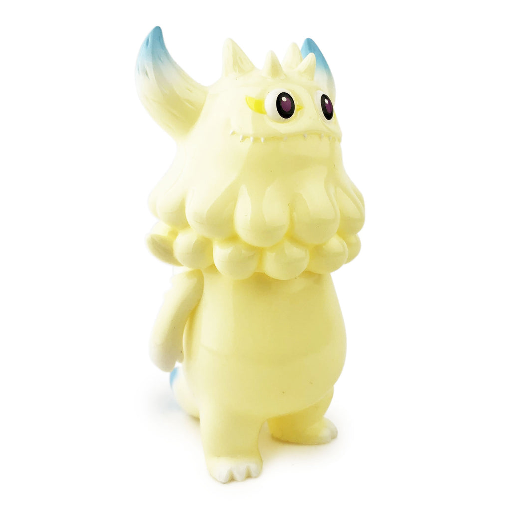 A small, pale yellow Rangeas Jr. — Halo figurine by The Little Hut (HK), featuring blue-tipped horns, three eyes, and a fluffy mane, stands upright against a white background.