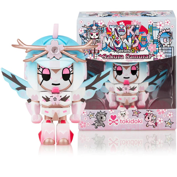 A tokidoki limited edition Tokimondo Series 2 Sakura Samurai figure in a pink and blue outfit stands in front of a box.
