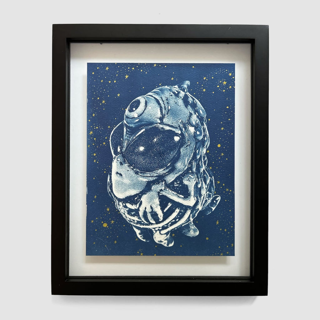 Alien Ghost 2 by Lindsay Wailes DiFabbio (EX102025-01), a framed artwork from Rotofugi, features a stylized one-eyed alien with a large head and hands set against a starry blue background.