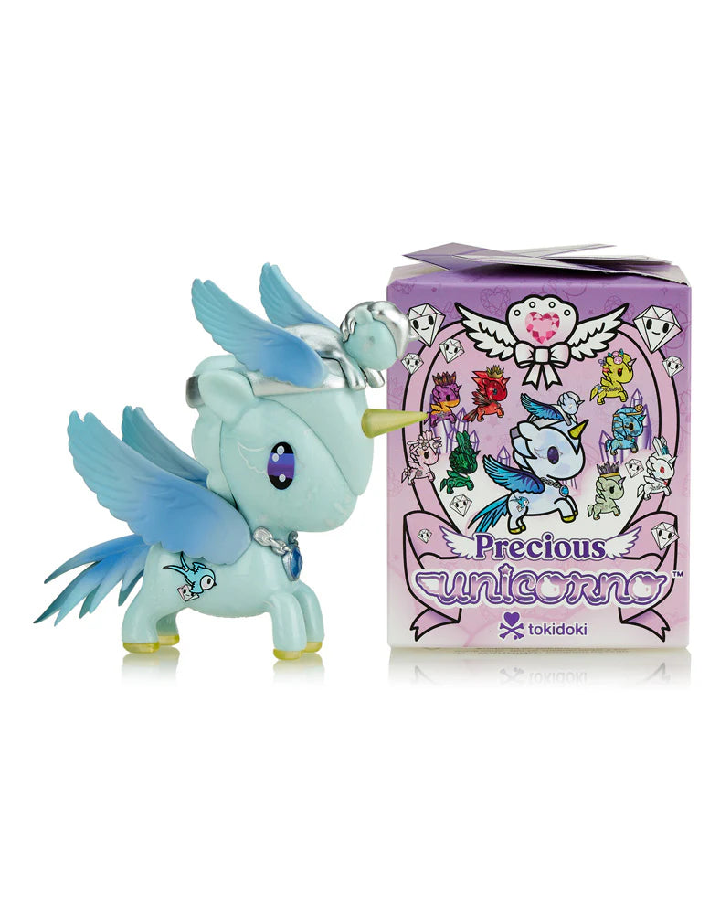 A blue unicorn with wings and a horn is beside a vibrant Tokidoki Precious Unicorno Blind Box by tokidoki, featuring various unicorn illustrations.