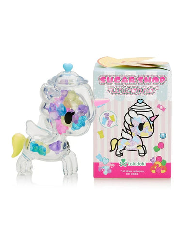 A clear unicorn figurine filled with colorful gems, resembling sparkling candy, sits next to the Tokidoki Sugar Shop Unicorno Blind Box displaying a matching unicorn illustration and Tokidoki brand logo.