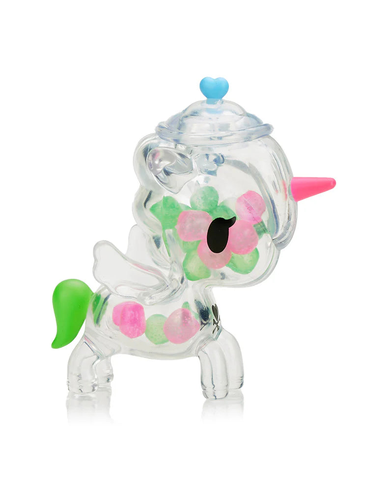 The Tokidoki Sugar Shop Unicorno Blind Box figurine boasts a clear design with a pink horn, green tail, and intricate flower patterns inside. It has a detachable lid topped by a blue heart, making it perfect for candy lovers who enjoy the magic of unwrapping surprises.