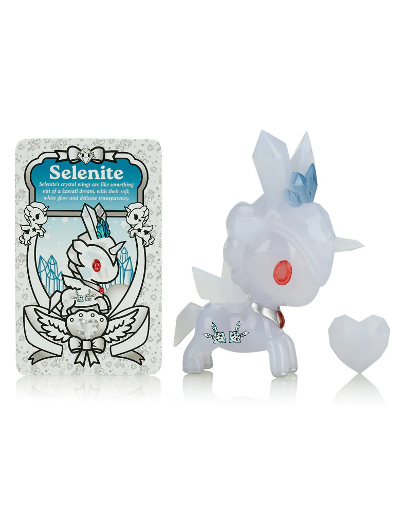 The Tokidoki Precious Unicorno Blind Box toy features a translucent white body with a blue crystal accent, accompanied by a heart-shaped object and a 