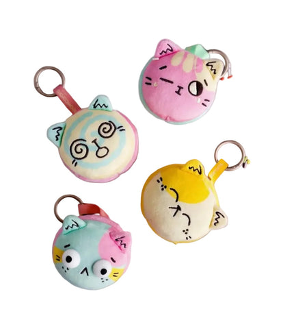 Four Meowcaron Plush Bag Charms by Kaleidos Creative, each with a unique facial expression, are arranged on a white background—perfect as adorable cat bag companions and cute plush keychains.