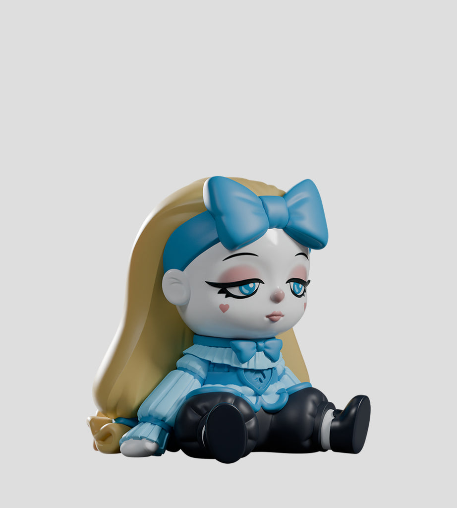 A vinyl doll from Kaleidos Creative’s A Mad Tea Party Blind Box, with long blonde hair, a big blue bow, blue sweater, black pants, and blue shoes sits on the ground with a neutral expression.