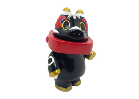 Akabegon- Black by Rotofugi is a black and gold cartoon figurine inspired by Akabeko, featuring a red scarf, round eyes, and animal-like features—a unique good luck charm designed by Teresa Chiba.