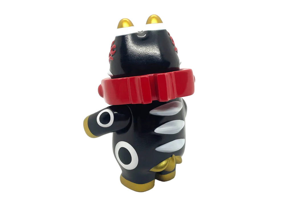 The Akabegon-Black by Rotofugi is a black vinyl figure inspired by Teresa Chiba's Akabeko, featuring gold accents, a red collar, and white eye and claw details—a charming good luck charm against a white background.