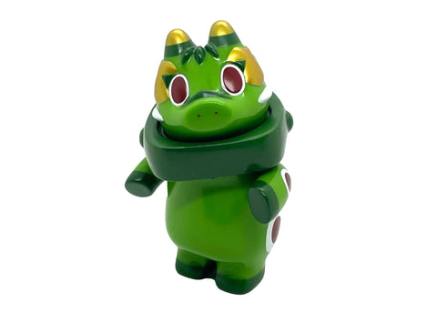 The Akabegon- Green Tea by Rotofugi is a dragon-like vinyl toy with gold accents, red eyes, and white spots, inspired by Teresa Chiba’s Akabeko cow. It stands upright against a plain background—a unique good luck charm for any collection.
