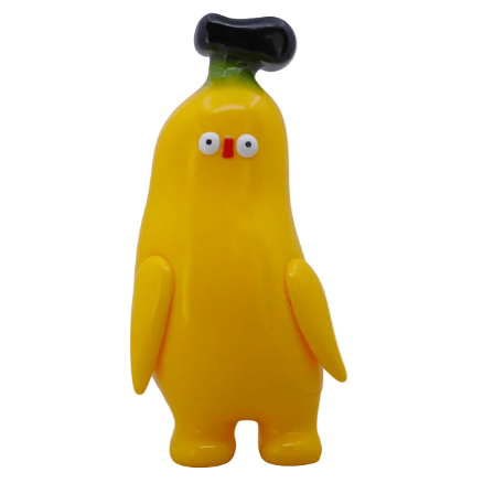 Banana Boo - Yellow by Rotofugi is a cute, banana-shaped plush collectible with small arms, wide eyes, a red nose, and a black-tipped head—standing upright against a plain background.