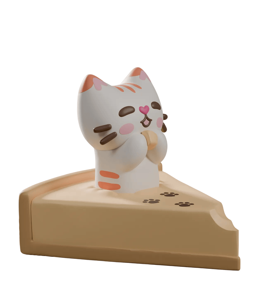 A smiling cat figurine with closed eyes sits on a cheesecake slice with paw prints and a missing bite, inspired by Bake Me A Cat Blind Box figures from Kaleidos Creative.