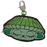 The Capkins Mystery Coin Bag by Kaleidos Creative is a collectible keychain with an embroidered green character featuring closed eyes and large ears, ideal for fans of blind box surprises or Capkins accessories.