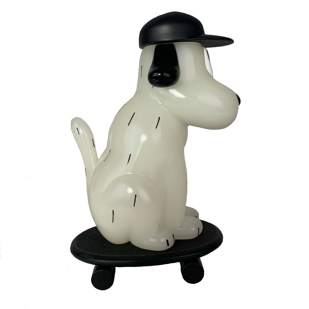 The One-Chu SK8 - Glow by How 2 Work is a white cartoon dog figurine with black spots and a black cap, sitting on a skateboard with wheels—plus, it features glow-in-the-dark details for extra fun.