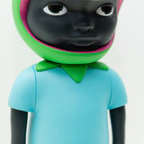 A close-up photo of a dark-skinned Phibby — OG (Green) vinyl figurine character by Hebru Brand (US), wearing a light blue shirt and a green and pink headpiece. The limited edition piece, inspired by Hebru Brantley, features a neutral expression.