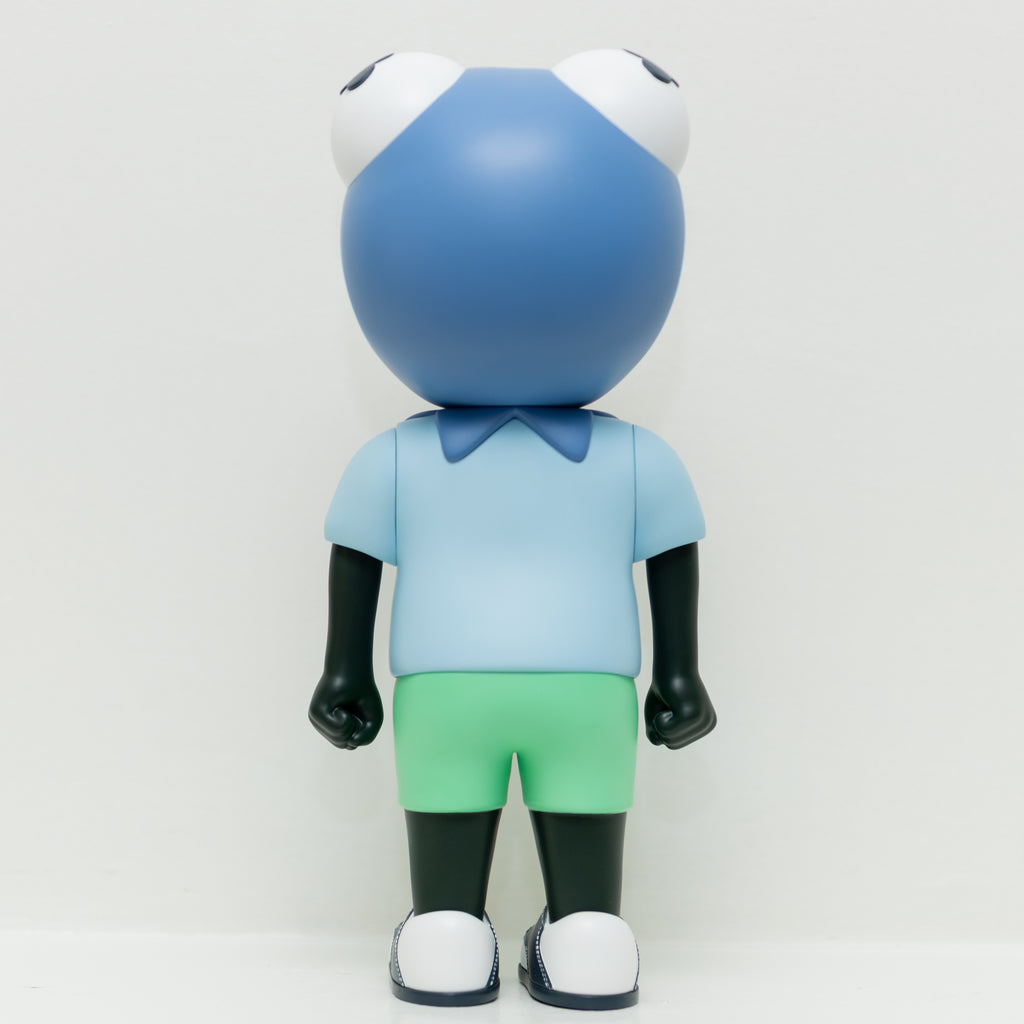 A figure named Phibby — Purple, featuring a frog-shaped head, a blue shirt, green shorts, and black limbs, stands facing away against a white background. This limited edition piece by Hebru Brand (US) beautifully captures the charm of Hebru Brantley's iconic characters.