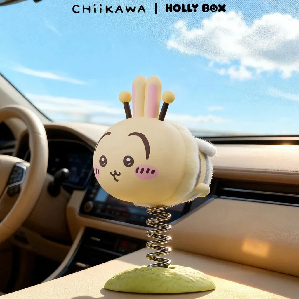 A small, round, light-yellow Chiikawa Little Bee Wobble Figure with rabbit ears and bee-like features, mounted as a wobble figure on a car dashboard.