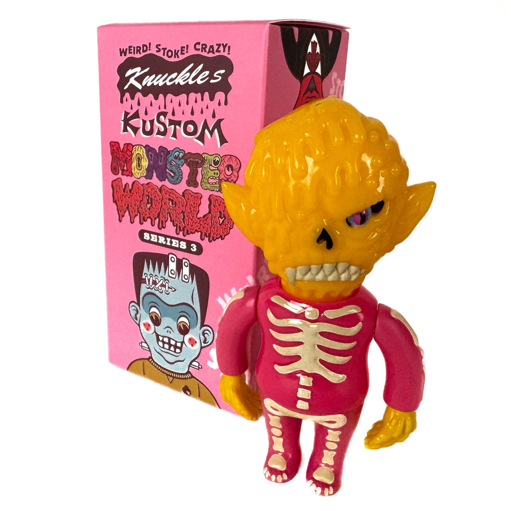 A yellow monster figurine with pointed ears and a pink skeleton body stands beside a pink 