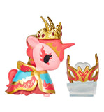 A pink Tokidoki Unicorno After Dark Masquerade Blind Box figurine wears a gold and red crown, blue and gold cape, and is displayed with a matching decorative headpiece beside it.