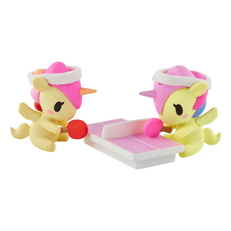 Two tokidoki Unicornos with pink manes play table tennis on a pink and white table, each with a red paddle—the Tokidoki Twinsies Unicorno Blind Box is perfect for collectors or as a fun tokidoki surprise.