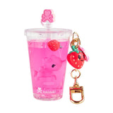 A clear cup from the tokidoki Beverage Besties Unicorno Blind Box shows pink liquid, a floating pink unicorn toy, a strawberry charm, and a gold keychain. 