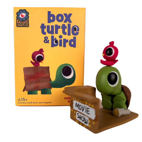 The Box Turtle & Bird Blind Box by Kaleidos Creative features a turtle figure holding a "Movie Show" sign, with a bird on its head. This charming magnetic collectible is recommended for ages 15+ and comes in surprise packaging.