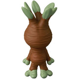 The Medicom VAG 46 — Mandoraguraki is a brown, root-like figure with three green-tipped branches on its head and a textured back, inspired by Japanese vinyl toy design and reminiscent of collectible gachapon figures.