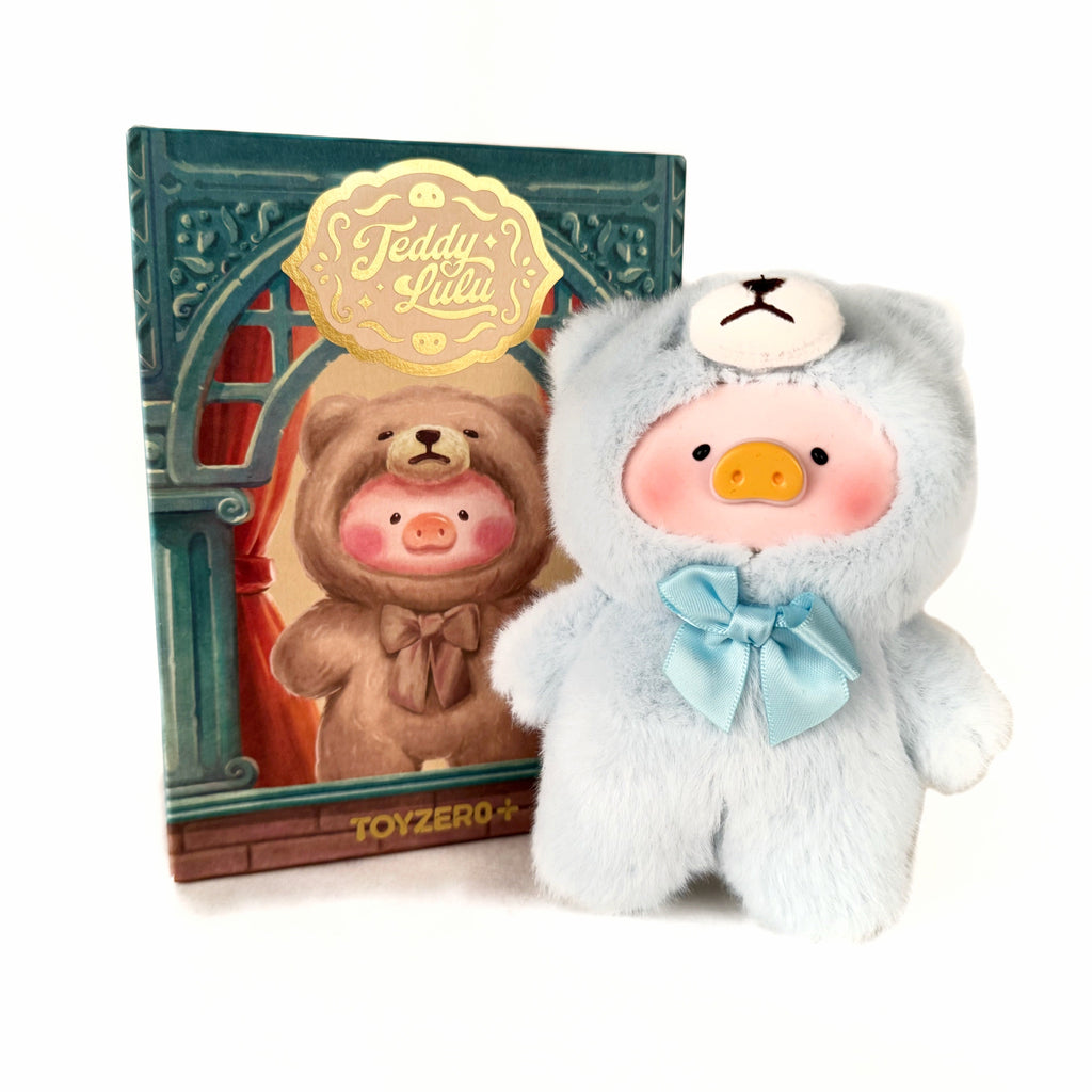 A light blue Lulu the Piggy plush in a bear hoodie with blue bow stands before a box illustrated with a similar plush. The Toyzero+ 