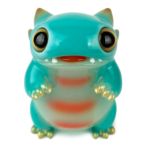 A teal monster figurine, "Tokke — Year of the Dragon (Glow)" from The Little Hut (HK), features large eyes, pointy ears, a striped pattern, and visible claws while standing upright.