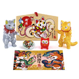 The Konatsuya 2025 Happy Set features vibrant Snake Cat Daruma figurines adorned with snake motifs, including a Konatsu illustration card, all elegantly set against a plain background.