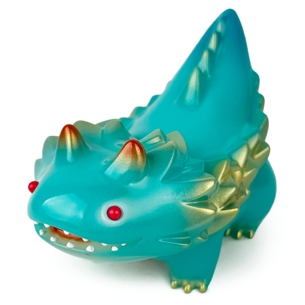 A teal toy figure, resembling a dinosaur or creature with red eyes and gold horn-like protrusions, is identified as the Seedlas Brother — Year of the Dragon (Glow) by Paradise Toy (TW).