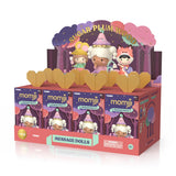 A Momiji — Sugar Plum Woods Blind Box display containing four collectible figures in message doll packages, topped with a cardboard cutout of three whimsical dolls in a forest setting.