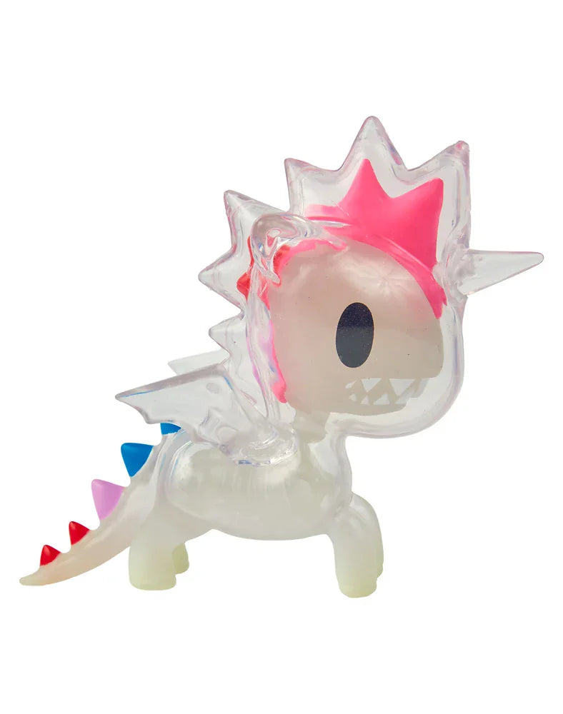 A translucent toy dragon from tokidoki’s After Dark Skeleton Unicorno Blind Box, featuring pink spikes, colorful tail spikes, big black oval eyes, and small white teeth, stands on four legs against a white background—just like a rare collectible discovery.