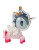 A small, clear plastic unicorn figurine from the tokidoki After Dark Skeleton Unicorno Blind Box collection, featuring pink legs, white wings, a gold horn and ears, a blue mane, and an eyepatch over one large eye. Reminiscent of classic Unicorno collectibles, its body is filled with sparkles and delicate flower details.