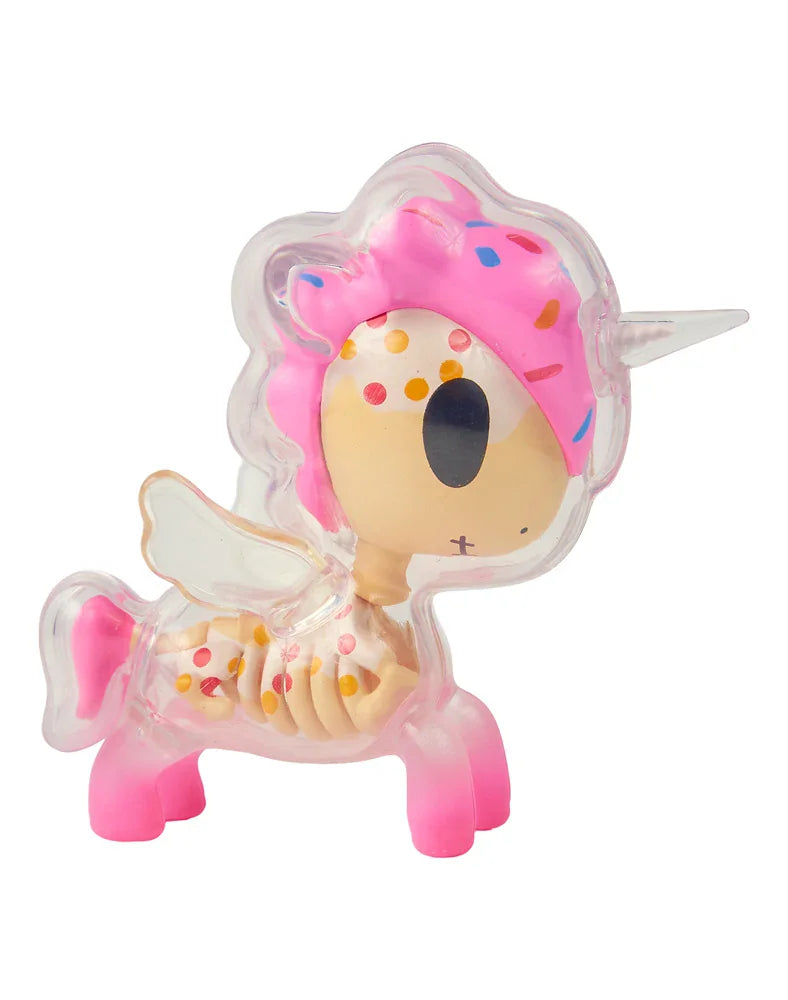 A transparent plastic unicorn figurine from tokidoki’s After Dark Skeleton Unicorno Blind Box collection, showcasing pink hooves, a white horn, wings, a mane resembling a pink frosted donut, and colorful sprinkles on its body—evoking the signature playful style of the Skeleton Unicorno series.