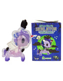 A translucent purple Skeleton Unicorno toy from tokidoki stands next to a tokidoki After Dark Skeleton Unicorno Blind Box, which is decorated with cartoon artwork, stars, and a moon.