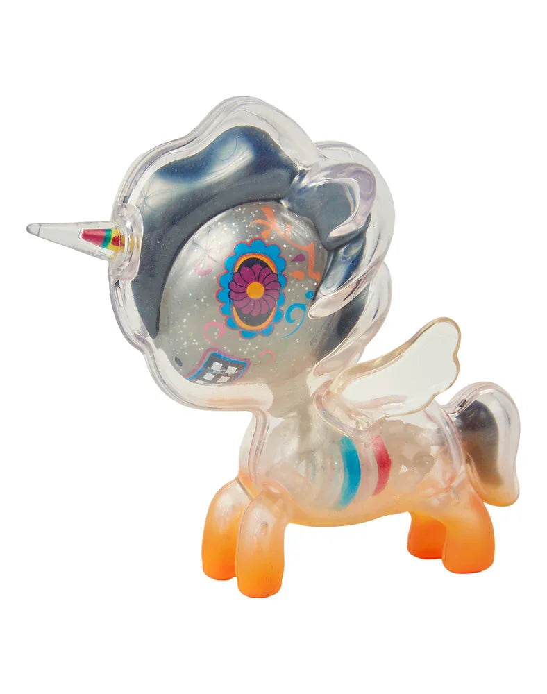 The After Dark Skeleton Unicorno - Caramelo (Special Edition) by tokidoki is a translucent unicorn figurine featuring a rainbow horn, wings, orange hooves, and vibrant designs across its face and body—complete with mesmerizing glow-in-the-dark accents for an enchanting display day or night.