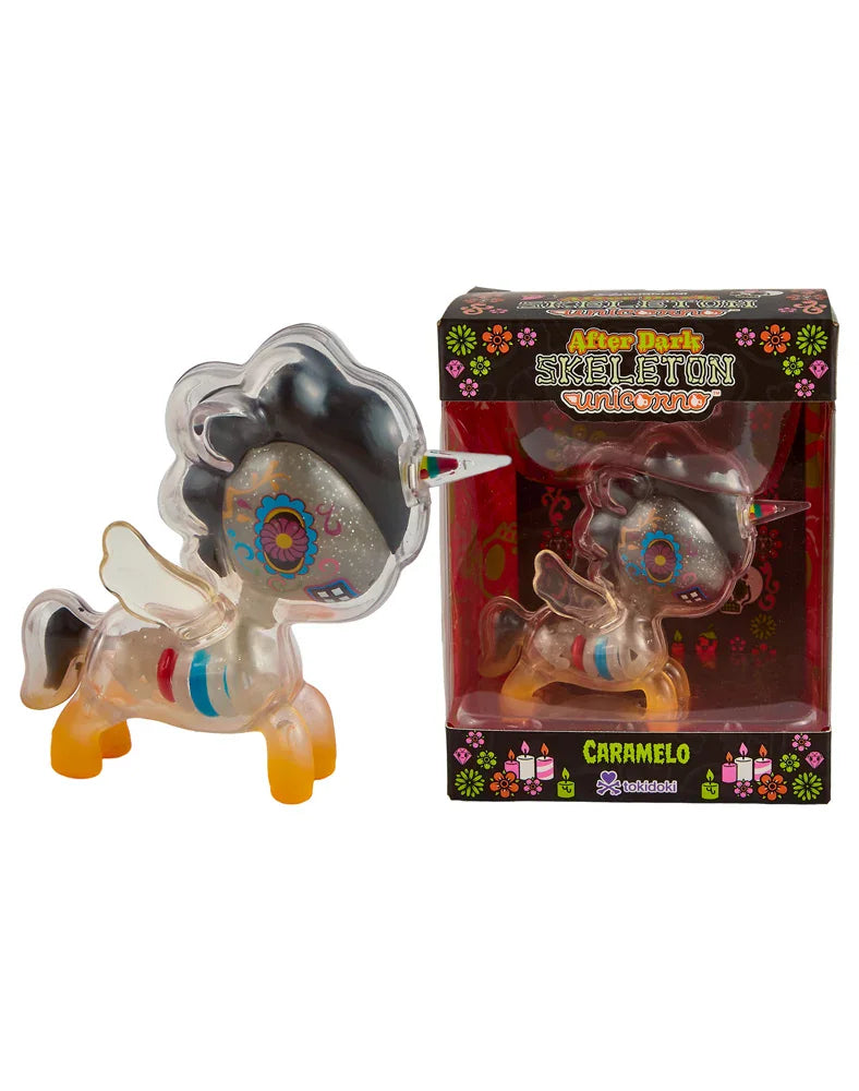A translucent tokidoki After Dark Skeleton Unicorno - Caramelo (Special Edition) figurine, featuring skeleton details and a vibrant design, is displayed beside its box. The packaging showcases vivid floral patterns and a window that reveals the glow-in-the-dark collectible inside.
