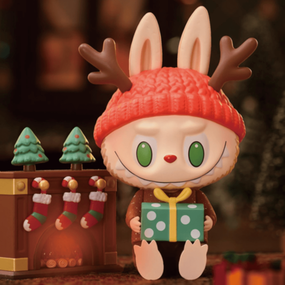 A toy bunny is holding a present in front of a Christmas tree decorated with festive costumes, featuring The Monsters - Let's Christmas Blind Box from Strangecat Toys (US).
