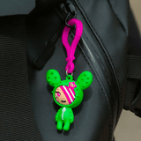 A green and pink Tokidoki Characters series 1 Blind Bag Clips teddy bear hanging from a backpack.