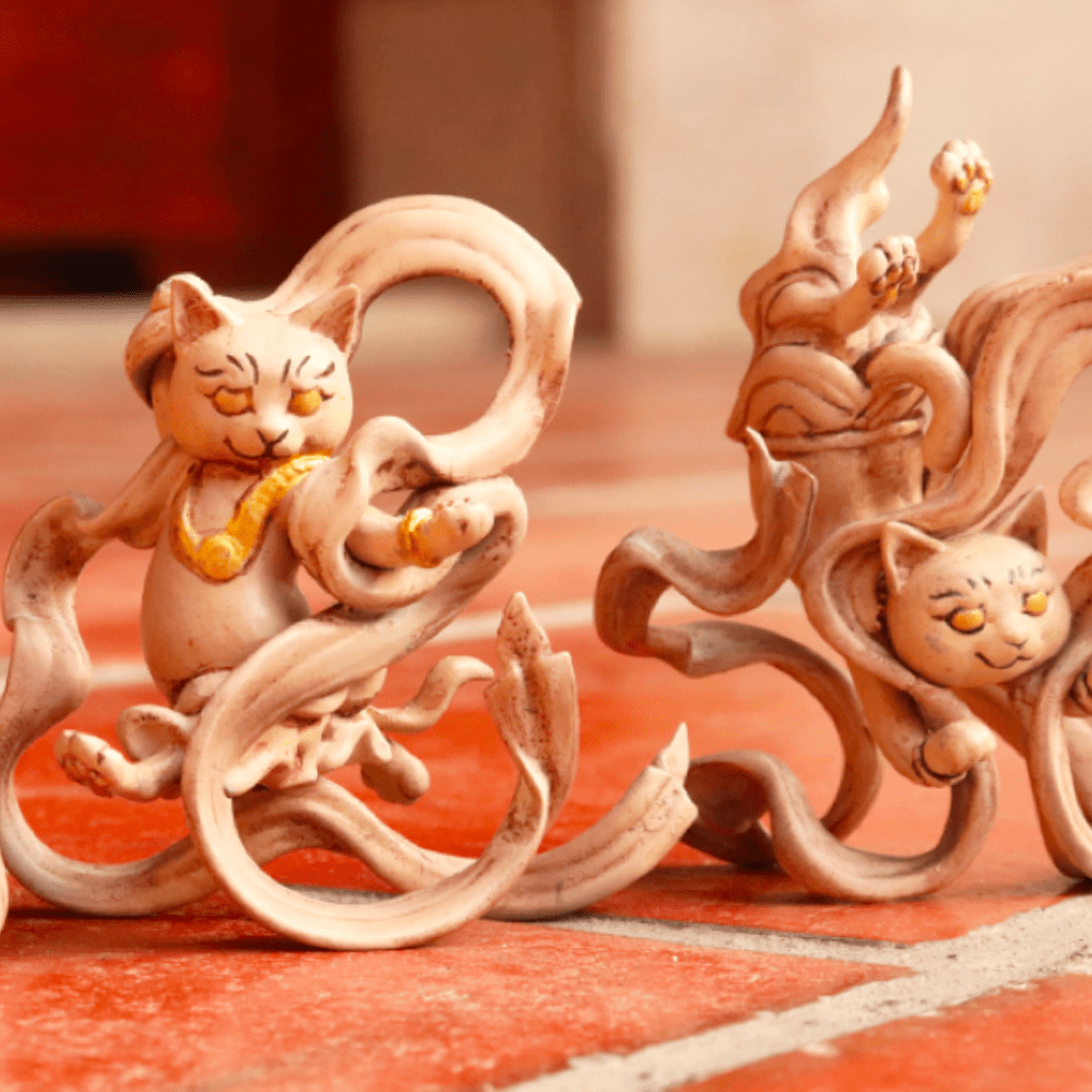 Two HitenNeko Flying Cat figurines sitting on a red tile floor.