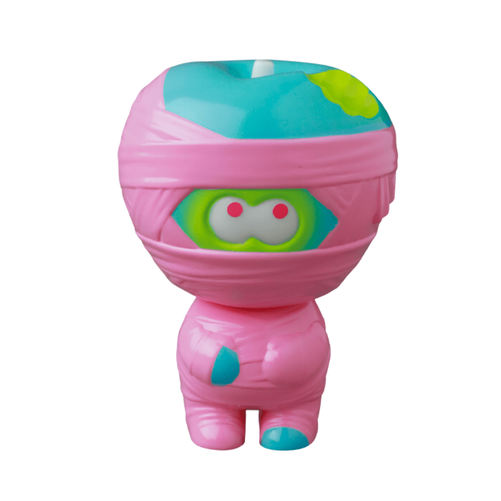 A small, colorful toy figure wrapped in pink bandages with green eyes peeking through. Resembling the charm of gachapon figures, VAG 36 - Yummy Mummy by Medicom (JP) has a blue and green top and a light blue spot on its lower front side, capturing the essence of Japanese vinyl toys.